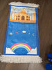 A blue prayer rug with colorful illustrations including a space station, a windmill, and what appears to be a stylized moon and stars pattern, placed on a wooden floor.