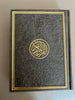 A black leather embossed Quran with gold trim, featuring the Arabic text and decorative design on the cover.
