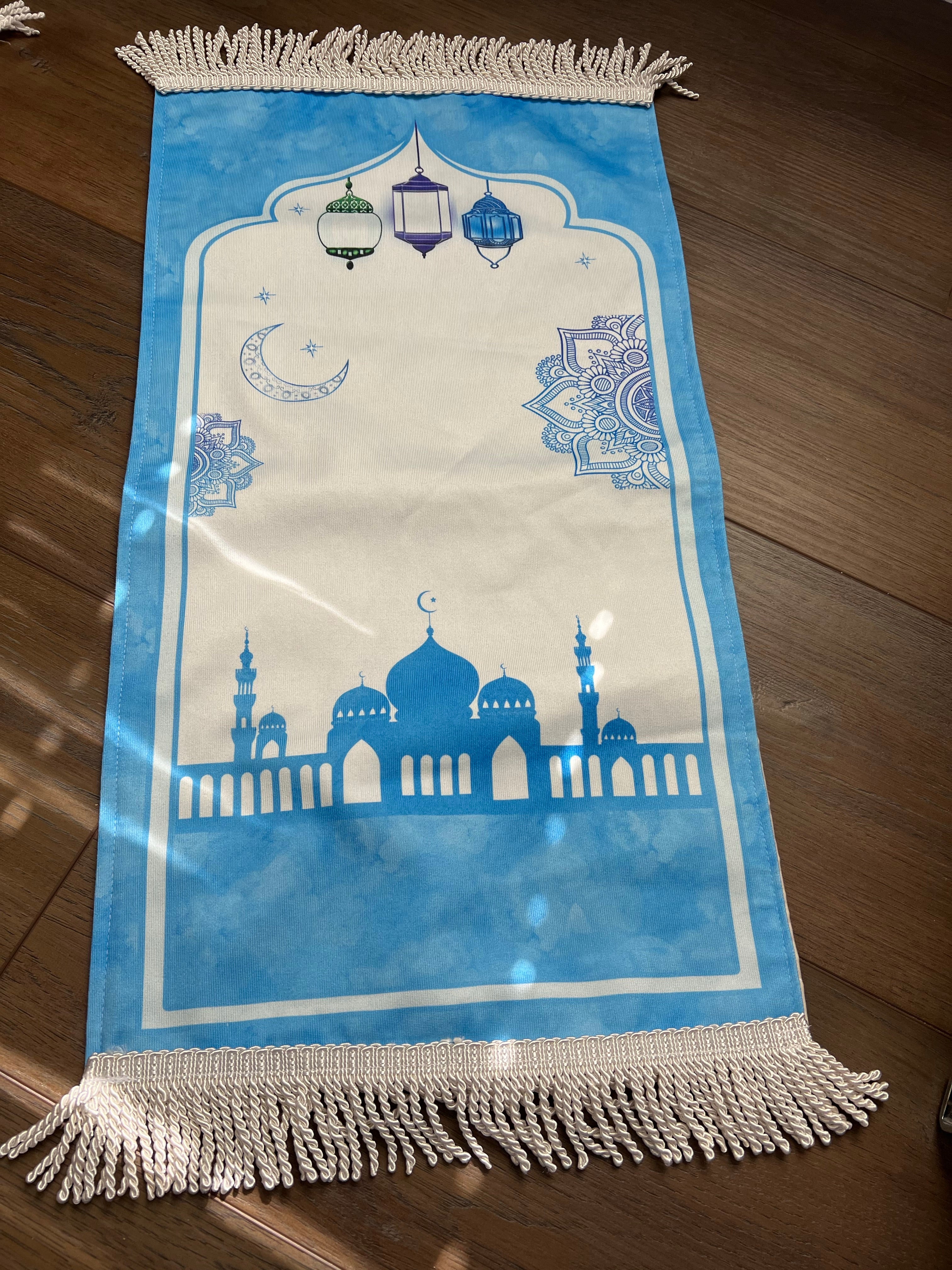 A blue and white prayer rug with religious patterns and text design, placed on a wooden floor.