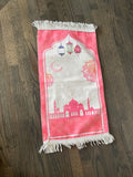 a pink prayer mat with detailed designs of flowers and the moon, with a mosque underneath
