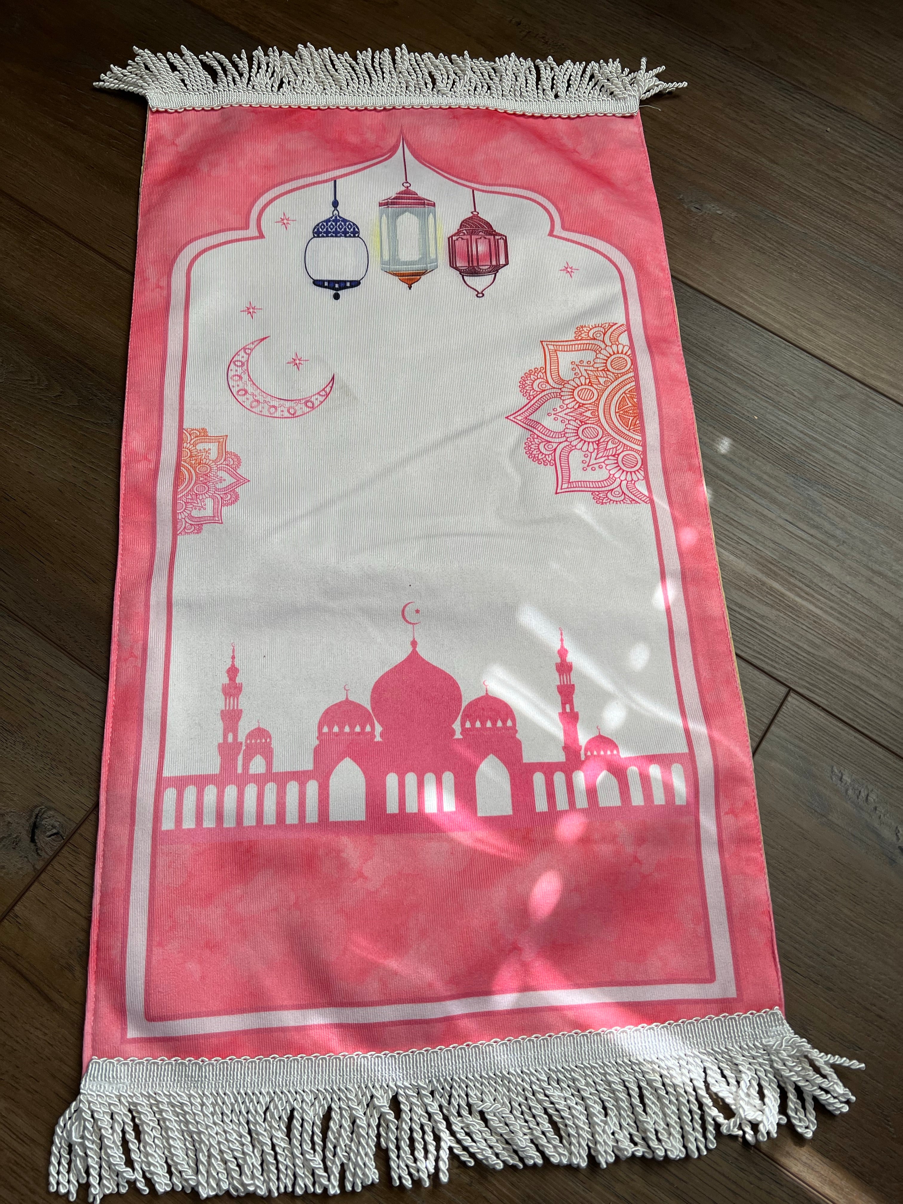 A light pink prayer rug featuring illustrations of a mosque, minaret, and stars.