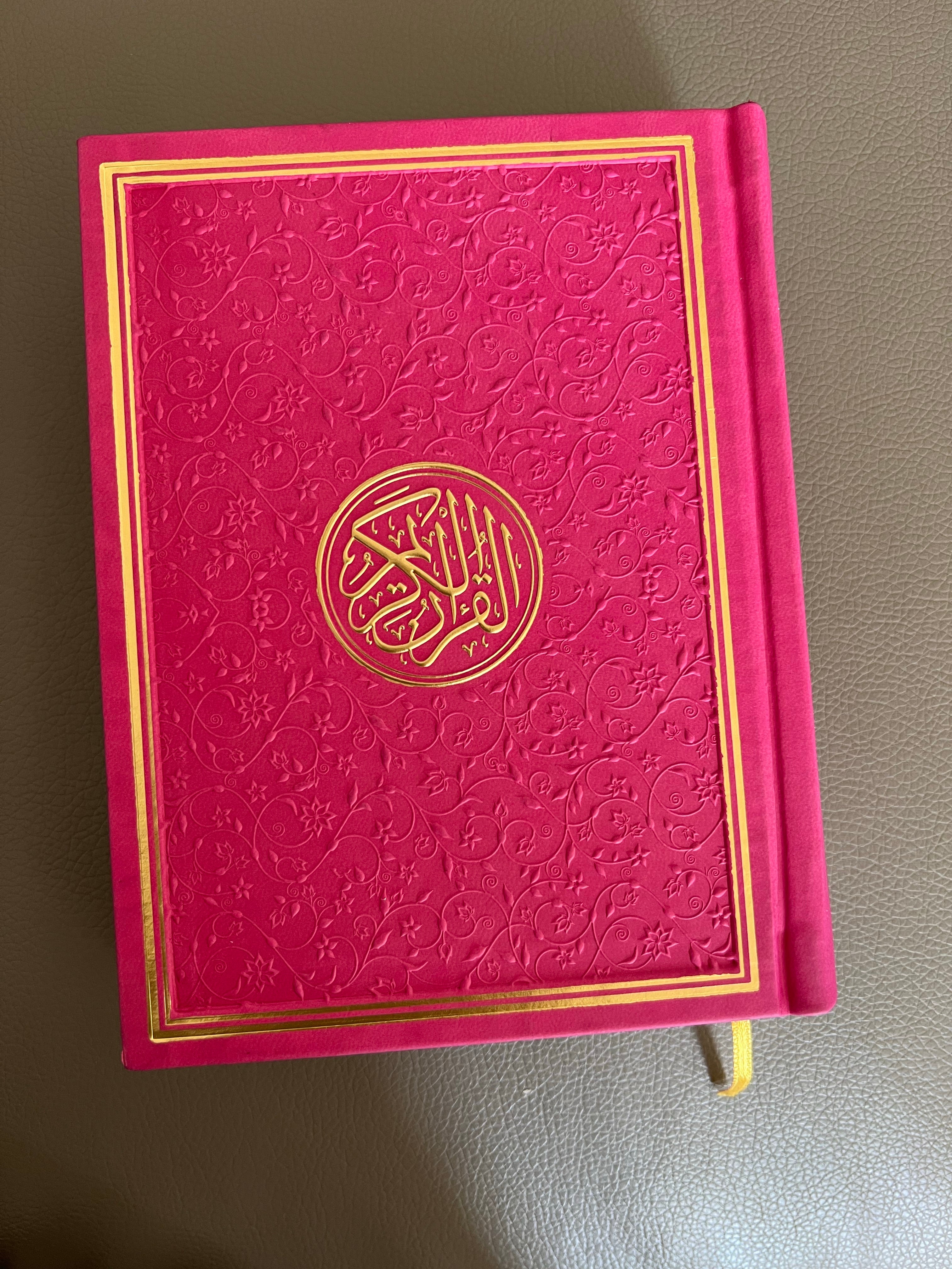 a pink quran with a gold trim, adorned with intricate design